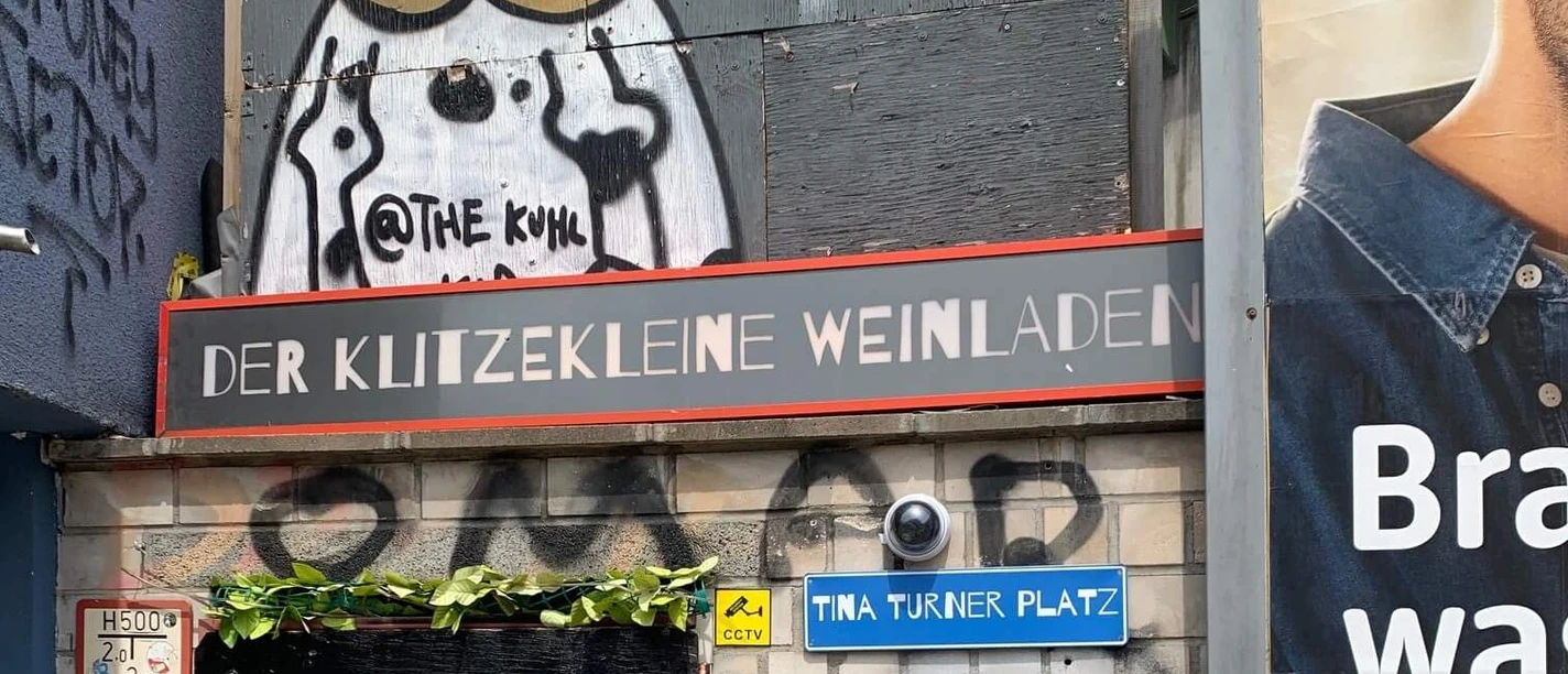 Der Klitzekleine Weinladen Fassade des Klitzekleinen Weinladens mit Graffiti-Kuh und Tina-Turner-Platz-Schild