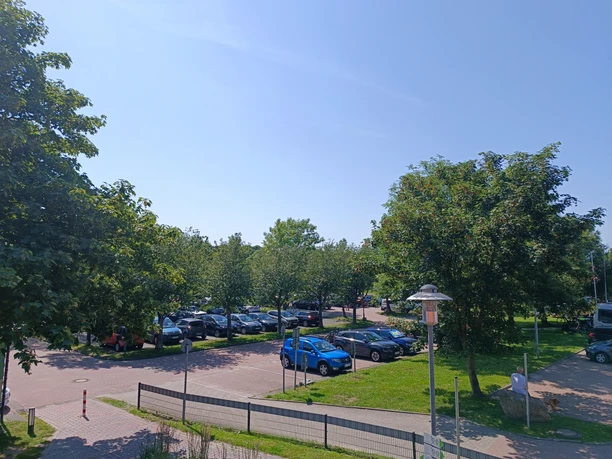 Parkplatz Ankerstraße Greetsiel.jpg Sonnige Aufnahme des Parkplatzes Ankerstraße in Greetsiel, gefüllt mit Autos unter grünen Bäumen.