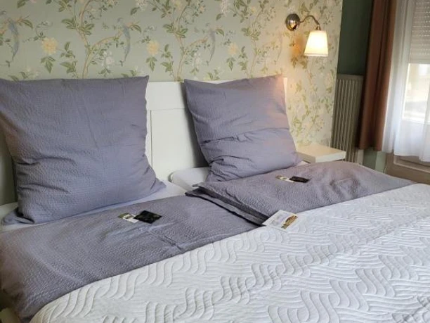 Privatzimmer2_Privatpension Waldbröl Doppelbett mit grauer Bettwäsche, floraler Tapete und Fenster im Privatzimmer