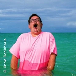 Mann im pinken Shirt steht im türkisfarbenen Wasser und ruft mit offenem Mund.