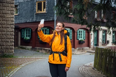 Waldarbeiterstube Frau in gelber Jacke macht ein Selfie mit ihrem Smartphone in einer malerischen Straße.