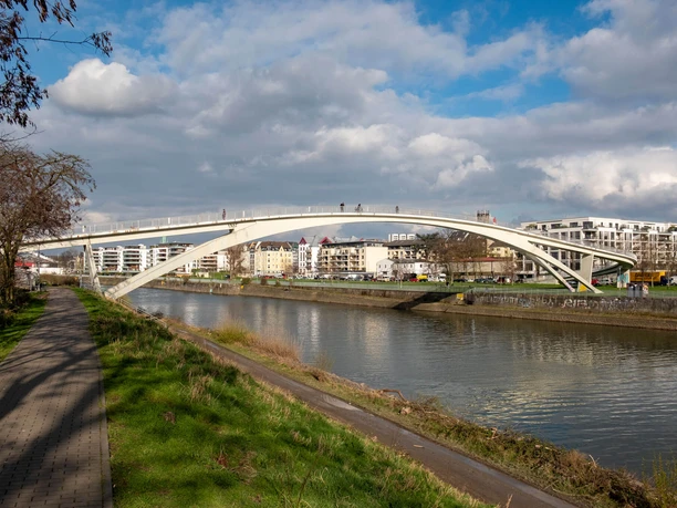 "Katzenbuckel Bridge" White arched bridge over the Mülheim Harbor with a riverside path and residential buildings