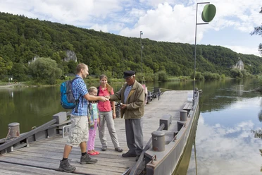 Auf der Gierseilfähre in Matting Vier Personen stehen auf einer Gierseilfähre über einem Fluss in einer grünen Landschaft.