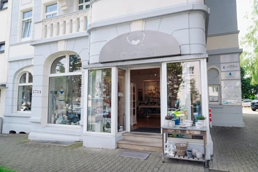 Herzensgut_Bad Wilhelmshöhe Der Eingang von dem Geschäft Herzengut in Wilhelmshöhe Kassel ist abgebildet. Das Gebäude ist grau & weiß, über der Tür hängt ein Schild mit der Beschriftung "Herzensgut".