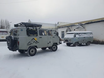 Zwei alte Vans stehen im Schnee vor einem Gebäude, einer mit Dachträger und Bergmotiv.