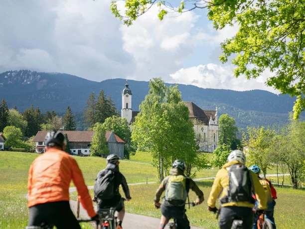 RadKultTouren Wieskirchrunde E-Bike Gruppe fährt durch grüne Voralpenlandschaft zur Wieskirche.