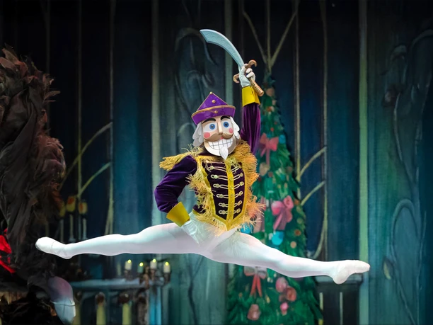 Der Nussknacker - GRAND CLASSIC BALLET Nussknacker-Tänzer springt mit Säbel vor märchenhafter Bühnenkulisse.