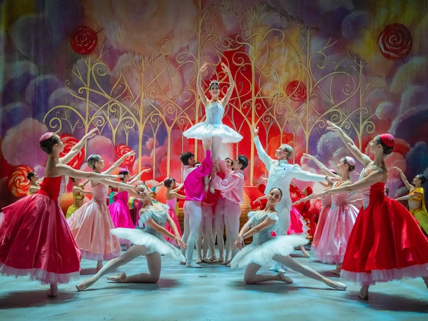Der Nussknacker - GRAND CLASSIC BALLET Ballettszene aus dem Nussknacker mit Tänzern in bunten Kostümen vor märchenhafter Kulisse