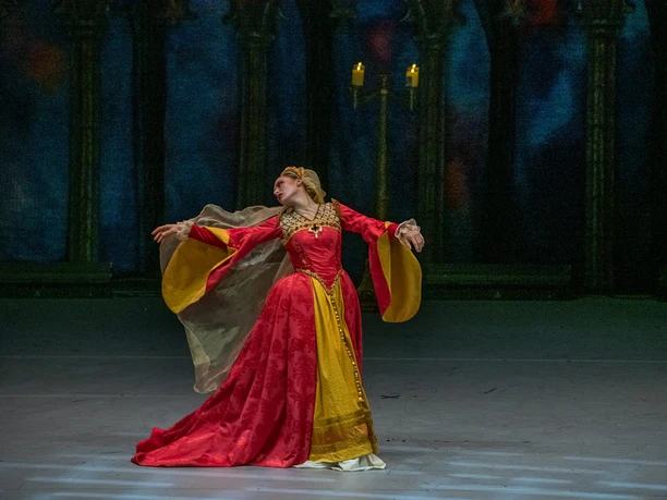 Swan Lake - Beyond the Stage A ballerina in a red-and-gold costume dances in candlelight against a dark stage backdrop
