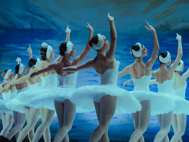 Schwanensee - Jenseits der Bühne Ballerinen in weißen Tutus tanzen Schwanensee vor blauem Bühnenbild