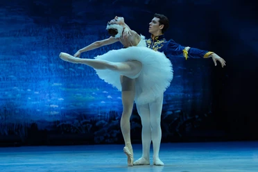 A ballet couple from *Swan Lake* against a glowing blue stage backdrop