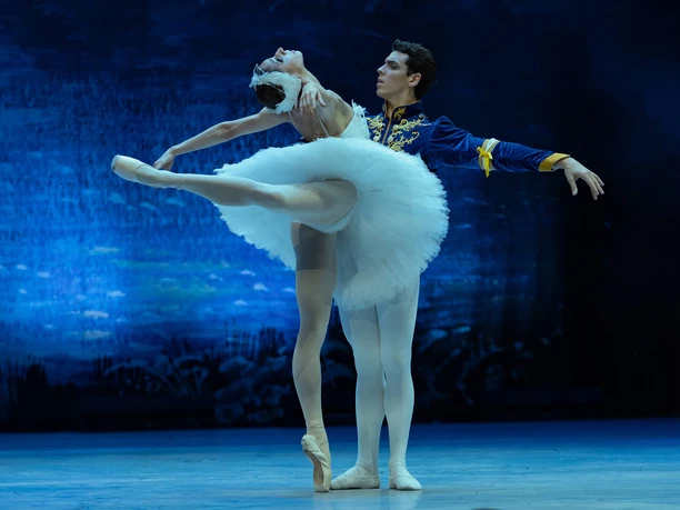 Swan Lake – GRAND CLASSIC BALLET A ballet couple from *Swan Lake* against a glowing blue stage backdrop
