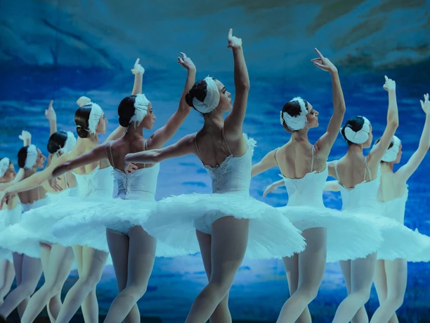 Swan Lake – GRAND CLASSIC BALLET Ballerinas in white tutus dance *Swan Lake* against a blue backdrop
