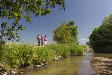 An der Großen Laber Drei Personen wandern entlang eines Flusses, umgeben von Bäumen und klarem Himmel.