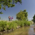 An der Großen Laber Drei Personen wandern entlang eines Flusses, umgeben von Bäumen und klarem Himmel.