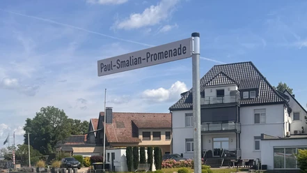 Schild mit schwarzer Schrift auf weißem Grund mit der Aufschrift "Paul-Smalian-Promenade"-