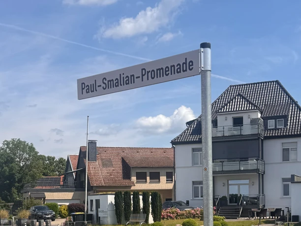 Schild mit schwarzer Schrift auf weißem Grund mit der Aufschrift "Paul-Smalian-Promenade"-
