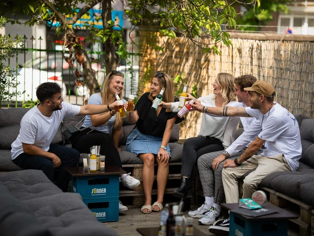 Beer Garden at BRAUWELT A group of friends clink bottles and beer glasses together at the BRAUWELT Cologne beer garden