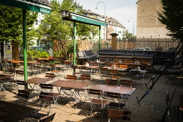 Beer Garden at BRAUWELT BRAUWELT's beer garden with wooden tables, benches, green awnings, and trees
