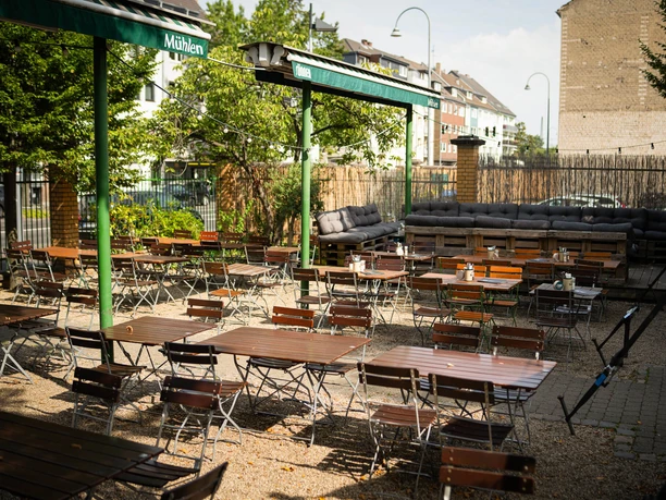 Beer Garden at BRAUWELT BRAUWELT's beer garden with wooden tables, benches, green awnings, and trees