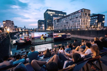 openairkino im Rheinauhafen Open-Air-Kino am Rheinauhafen mit Publikum auf Stufen und Leinwand auf dem Wasser