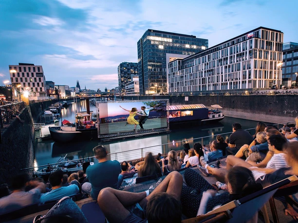 openairkino im Rheinauhafen Open-Air-Kino am Rheinauhafen mit Publikum auf Stufen und Leinwand auf dem Wasser