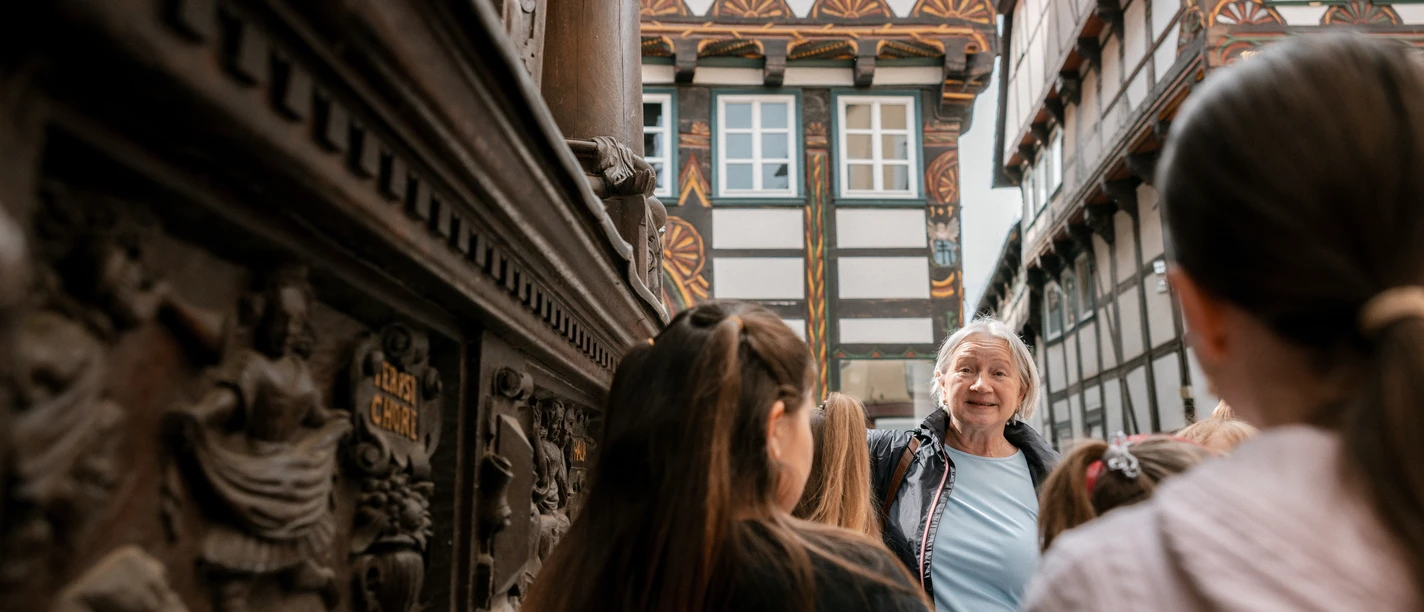 Stadtführerin erzählt Kindern von Fachwerkhäusern Stadtführerin erzählt Kindern vor verzierten Fachwerkhäusern in Einbeck.