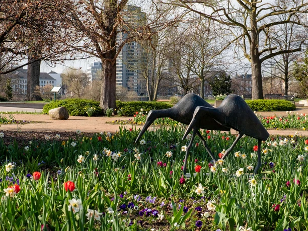 Rheinpark Skulptur im Blumenbeet des Kölner Rheinparks mit Bäumen und Hochhäusern im Hintergrund