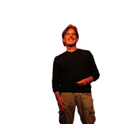 Wim Alexander smiles in the stage lights, wearing a black shirt and brown cargo pants
