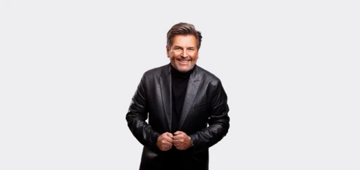 Thomas Anders lächelt in schwarzer Lederjacke vor hellem Hintergrund