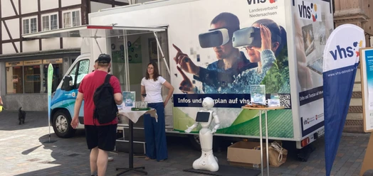 DigiMobil der vhs mit VR-Motiv, Infostand und Besucher auf einem Marktplatz