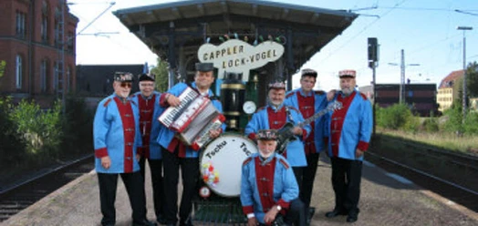 selected_csm_cropmiddle_Lockvoegeln_4496a4c832.jpg Musikgruppe in blauen Uniformen mit Akkordeon und Trommel vor einer historischen Lok
