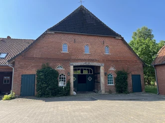 Komm ins Nest Roter Backsteinhof mit grünem Tor, kleinen Rundbogenfenstern und hohem Ziegeldach.
