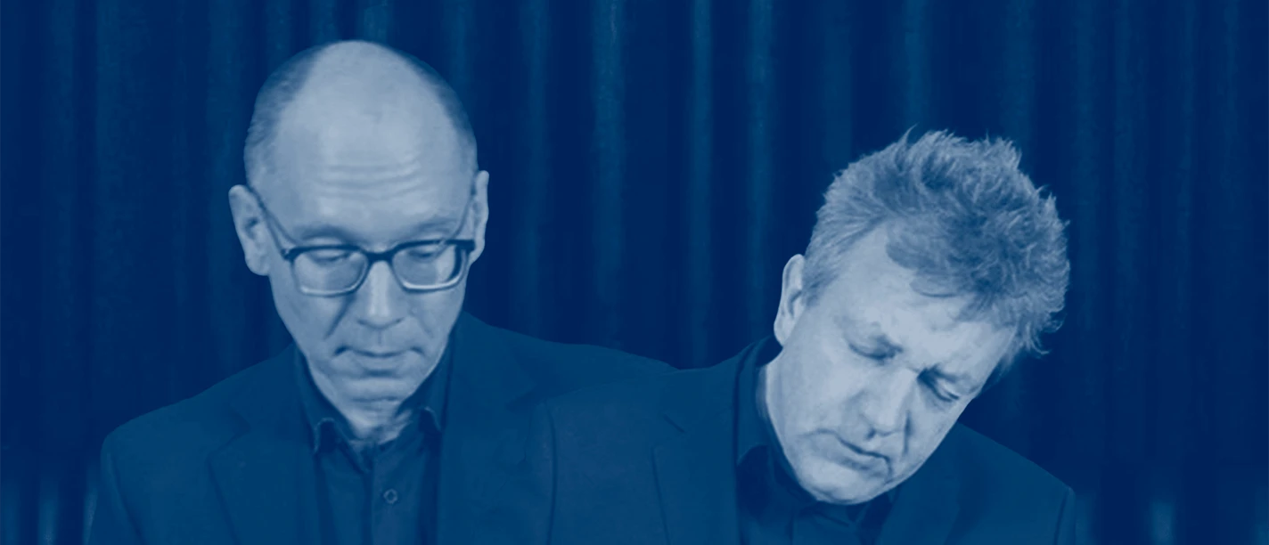 Tobias Koch and Benjamin Kobler Two musicians, deep in thought, wearing dark suits, in front of a blue stage curtain