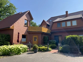 FeWo Heike Heitmann (7).jpeg Backsteinhaus mit gelber Tür, Balkon, Vorgarten und schmiedeeisernem Zaun.