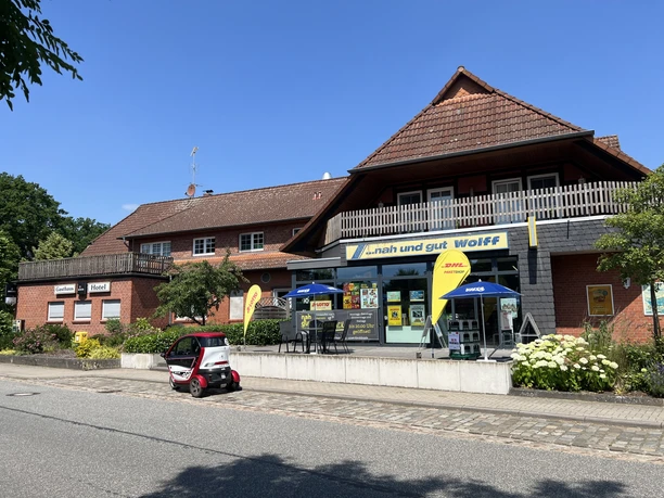 Hotel-Gasthaus zur Linde (4).jpeg Hotel-Gasthaus Zur Linde mit rotem Backsteinbau und Ladenfront an sonniger Dorfstraße.