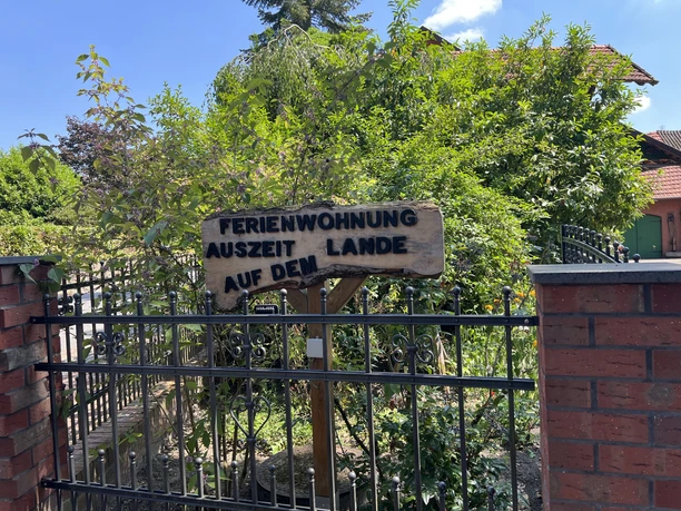 Houten bordje van het vakantieappartement ‘Auszeit auf dem Lande’ achter een zwarte tuinpoort.