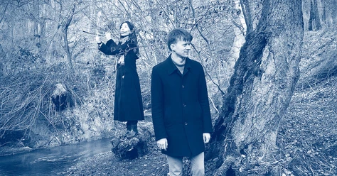 Blau getöntes Duo-Porträt: Flötistin und Musiker an einem Bach im winterlichen Wald