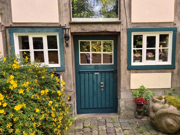 Grüne Haustür eines Fachwerkhauses mit weißen Fenstern und gelbem Blütenstrauch.