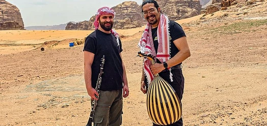 Zwei Musiker mit Kufiya und Instrumenten in einer Felswüste Jordaniens