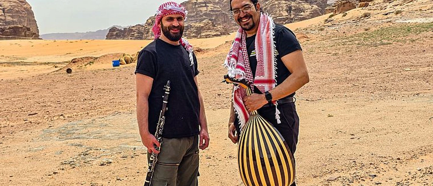 Zwei Musiker mit Kufiya und Instrumenten in einer Felswüste Jordaniens