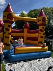 Hüpfburg.jpeg Kinder spielen auf einer gelb-roten Hüpfburg in Burgenform unter blauem Himmel.
