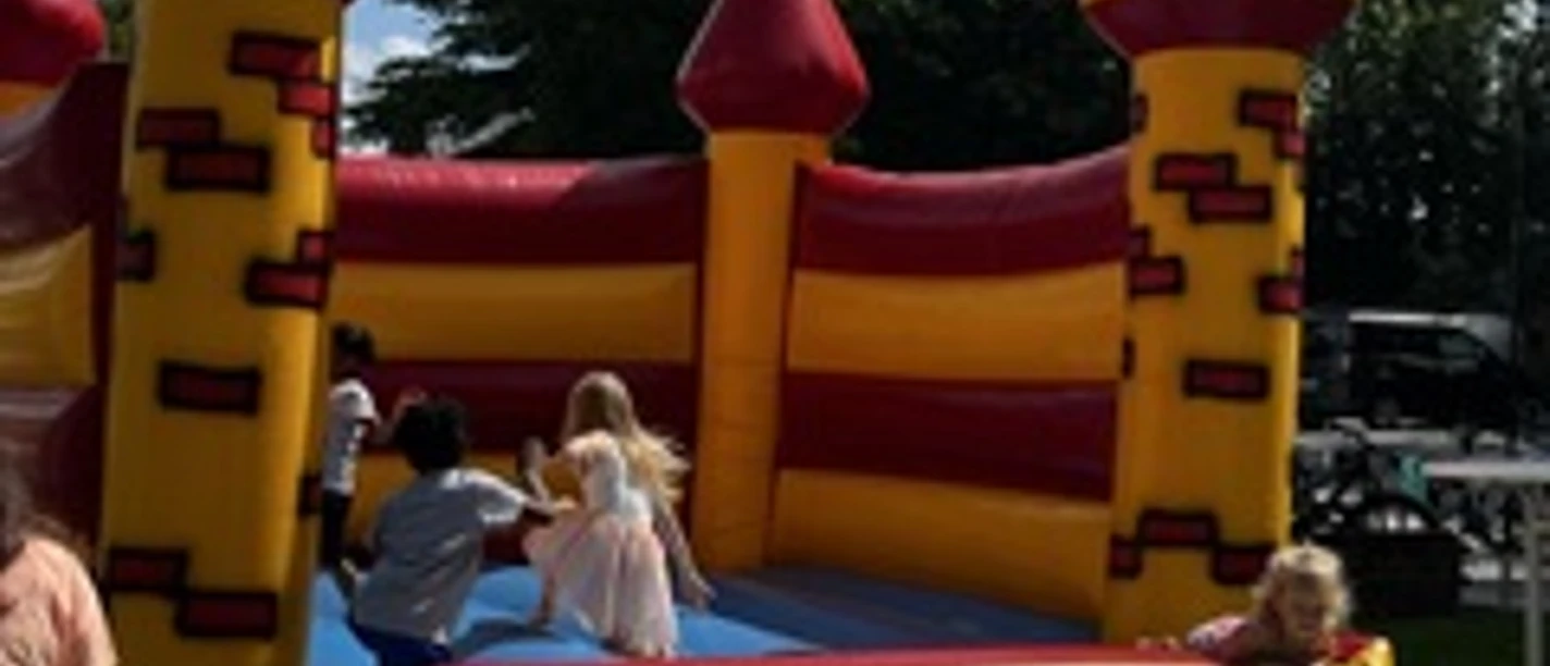 Hüpfburg.jpeg Kinderen spelen op een geel-rode springkasteel in de vorm van een burcht onder een blauwe hemel.