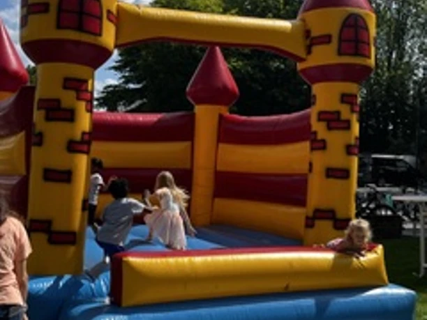 Hüpfburg.jpeg Kinder spielen auf einer gelb-roten Hüpfburg in Burgenform unter blauem Himmel.