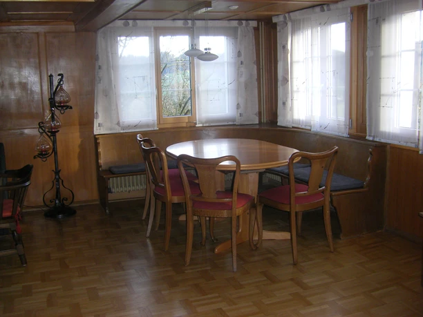 Gemütlicher Essbereich mit Holztisch, Stühlen und Eckbank vor grossen Fenstern in einer rustikalen Ferienwohnung