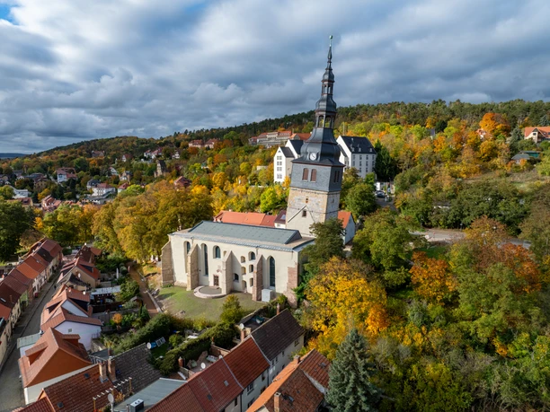 Blick auf den Schiefen Turm Schiefer Kirchturm von Bad Frankenhausen über herbstlichen Bäumen und roten Dächern.