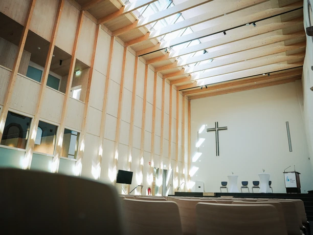Kirchenschiff im Schiefen Turm Helles Kirchenschiff mit Holzbalken, Sitzreihen und Kreuz im Schiefen Turm.
