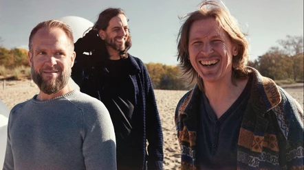 Drei Musiker des Emil Brandqvist Trio lachen am sonnigen Strand.