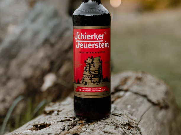 En 0,7-liters flaske Schierker Feuerstein står på en forvitret træstamme foran en sløret naturkulisse.
