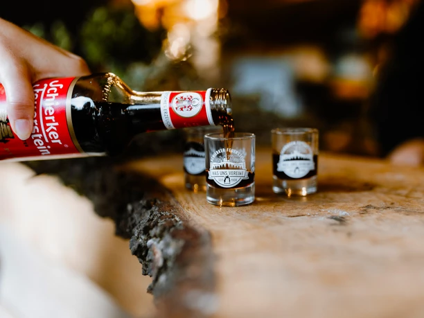 The Schierker Feuerstein herbal semi-bitter liqueur is poured into small glasses on a wooden table.